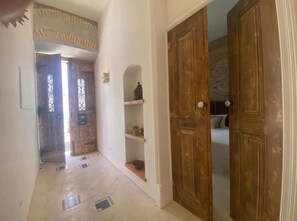 A hallway with a wooden door, a shelf with items, and a window with decorative elements. - Casa Amanhada - Apartment Zero (Grândola)