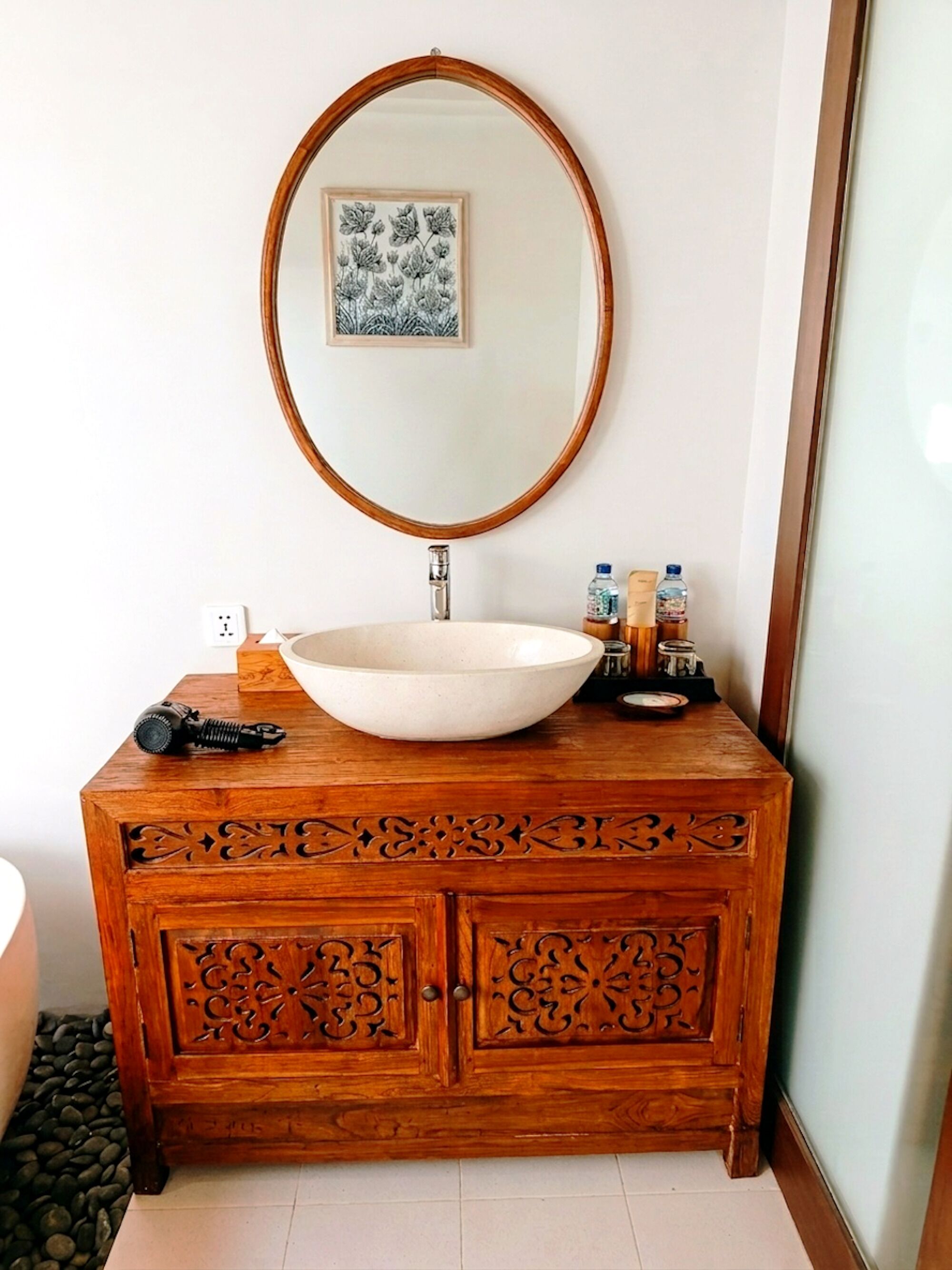 A wooden vanity with a large oval mirror, a white sink, and a decorative cabinet below.