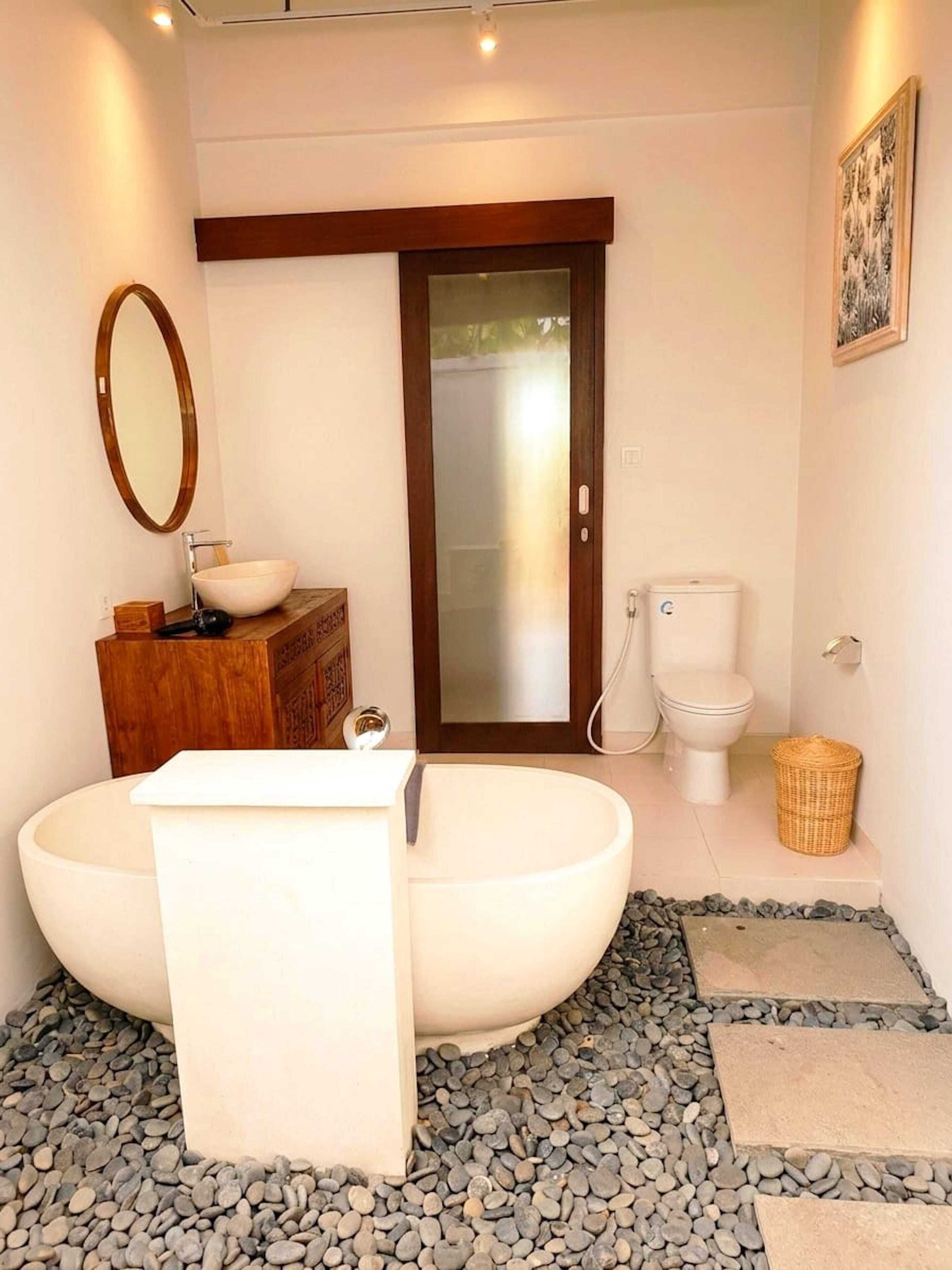 Um banheiro moderno com uma banheira independente, um móvel de vaidade em madeira, um espelho grande e um vaso sanitário.