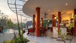 Een restaurant met bakstenen pilaren, houten tafels en een bar.