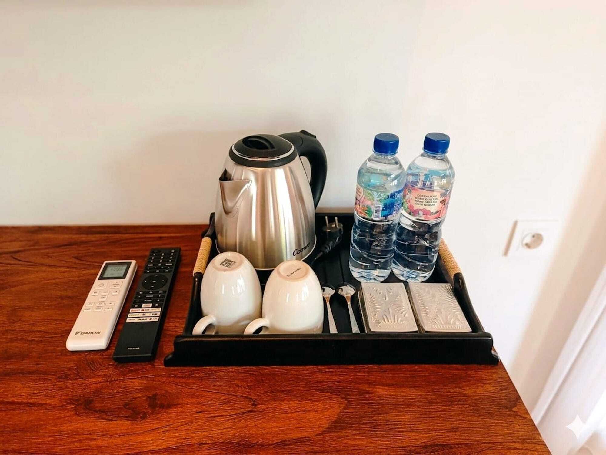 Un piano di lavoro in cucina con una macchina del caffè, due bottiglie d'acqua, un bollitore, un telecomando e un vassoio con tazze e un coltello.