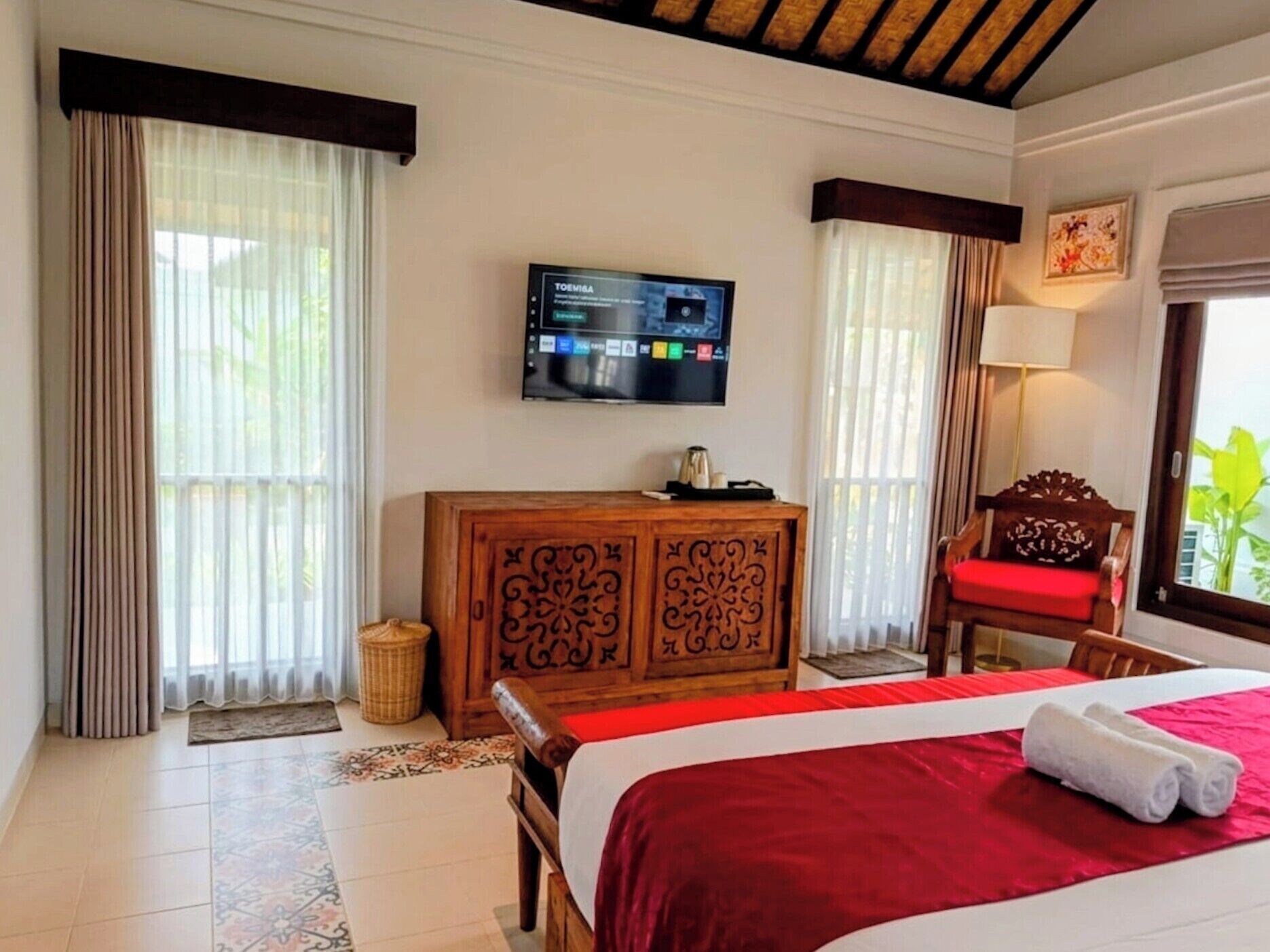 Una habitación de hotel con una cama, un televisor montado en la pared, un armario de madera y una ventana con cortinas.