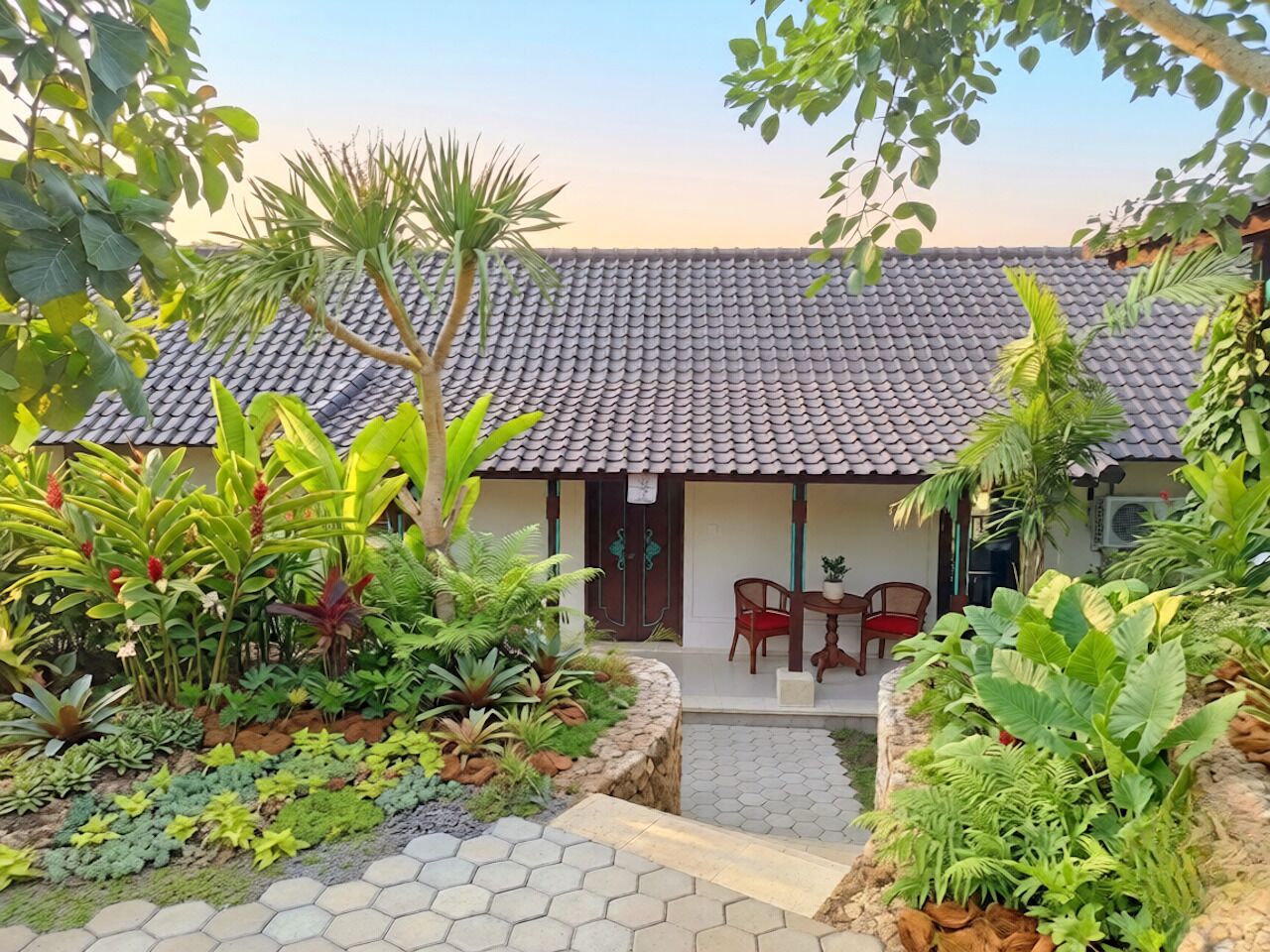 Een huis met een pannendak, omringd door een tuin met verschillende planten en een geplaveid pad.