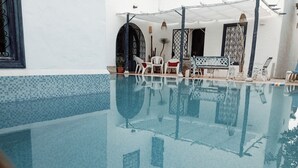 A pool with clear water, white walls, and a tiled floor. There are chairs and a bench around the pool. - Stylish villa in yasmine hamamet tourist zone, 5 min from carthage lind park. (Yasmine Hammamet)