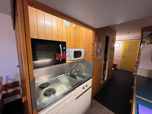 Une cuisine compacte équipée d’un four à micro-ondes, d’un petit évier et de panneaux muraux en bois.