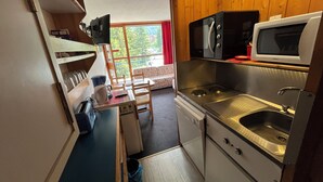 Uma cozinha compacta equipada com micro-ondas, fogão, pia e uma pequena área de refeições com mesa e cadeiras.
