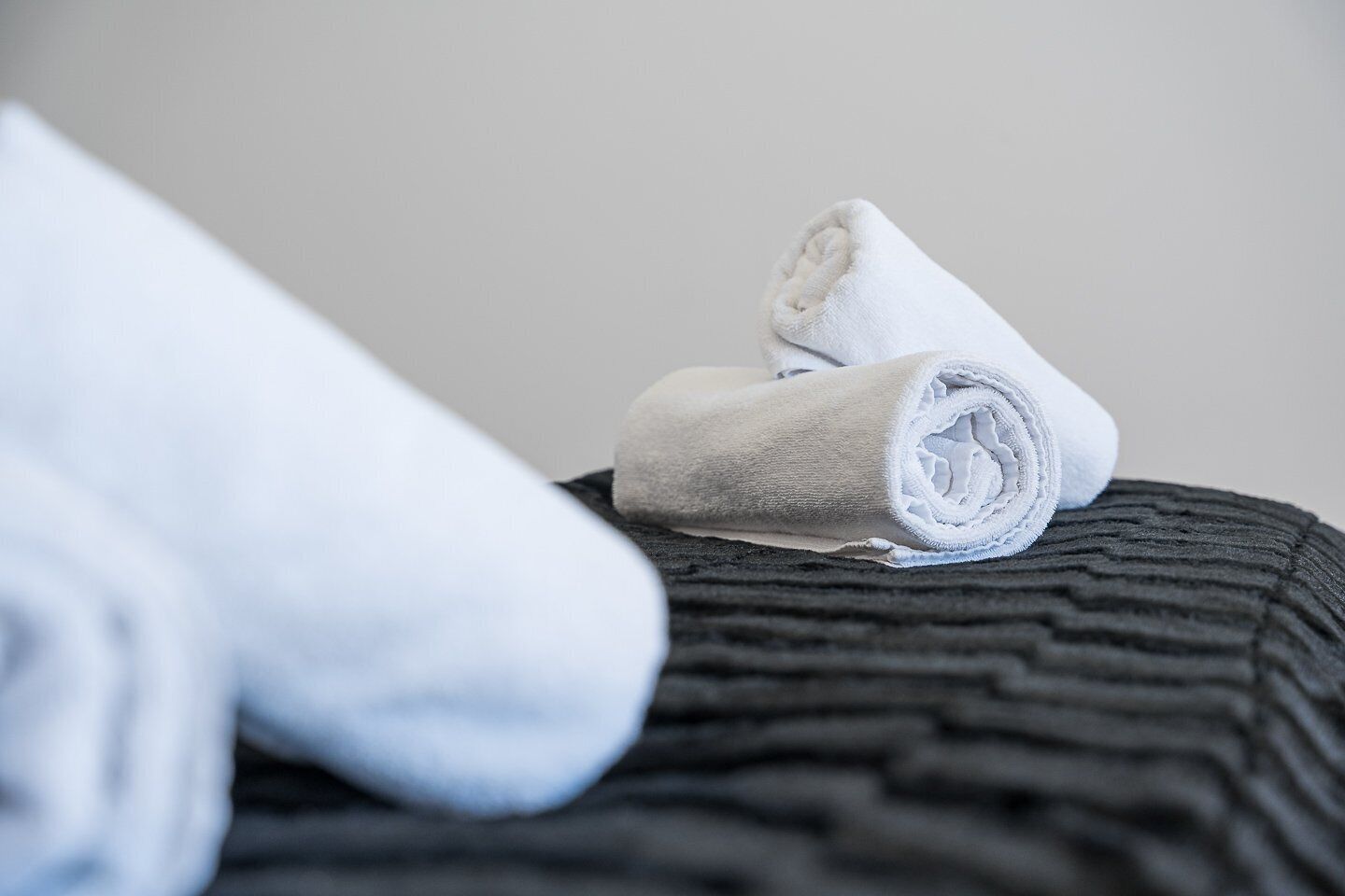 Une serviette blanche enroulée, posée sur un coussin noir à texture.