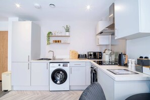 A modern kitchen with white cabinetry, a built-in washing machine, a coffee machine, and a microwave. - Modern & Spacious 1 Bedroom Preston Apartment (Preston)