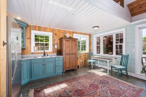Une cuisine avec des armoires de couleur turquoise, une armoire en bois, un réfrigérateur et un coin repas comprenant un banc et des chaises.