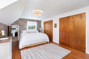 A bedroom with a sloped ceiling, a large bed, wooden wardrobe, and a stone accent wall. - Shalom at Shenandoah | Pool, Sauna & Views (Swoope)