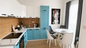 Une cuisine compacte avec des meubles blancs et bleus, une cuisinière encastrée et un coin repas avec des chaises et une table blanches.