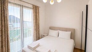 Une chambre d’hôtel avec un lit, une table de chevet, une vue sur les immeubles par la fenêtre et un luminaire au plafond.