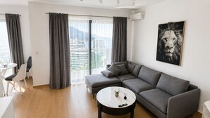 Un salon moderne avec un canapé gris, une table basse ronde et une vue sur la ville grâce à de grandes fenêtres.