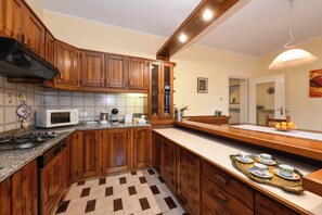 A kitchen with wooden cabinets, a microwave, a stove, and a dining area with a table set for tea. - Casa Nonna Rina: Enchantment and Relaxation among the Hills 15km from Lake Garda (Castellaro Lagusello)