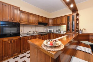 A kitchen with wooden cabinets, a microwave, a stove, and a large island with a woven placemat. - Casa Nonna Rina: Enchantment and Relaxation among the Hills 15km from Lake Garda (Castellaro Lagusello)