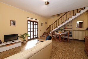 A living room with a sofa, TV, and a staircase leading to another level. - Casa Nonna Rina: Enchantment and Relaxation among the Hills 15km from Lake Garda (Castellaro Lagusello)