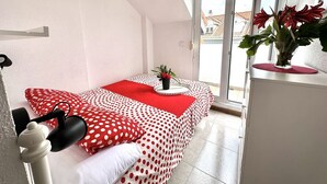 A room with a bed covered in polka dot bedding, a small table with a plant, and a window with a view of buildings. - Beachfront duplex - La Arena 4608 (Isla)