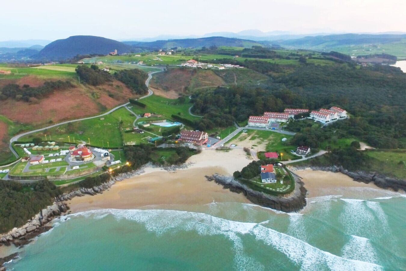 An aerial view of a coastal resort with multiple buildings, a beach, and a rocky shoreline.
