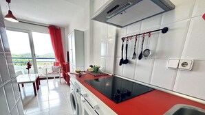 A modern kitchen with a red countertop, a built-in oven, a washing machine, and a large window with a red curtain. - Beachfront duplex - La Arena 4608 (Isla)