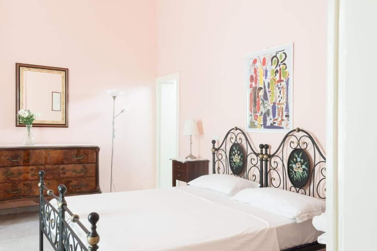 A bedroom with a bed, dresser, mirror, lamp, and artwork.