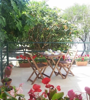 Eine Terrasse im Freien mit Tisch und Stühlen, umgeben von Blumentöpfen und Bäumen.