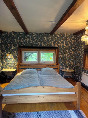 A bedroom with a wooden bed, two windows, a chandelier, and floral wallpaper. - Beautiful Swedish vacation home on the shore of a lake with complete privacy (Järnforsen)