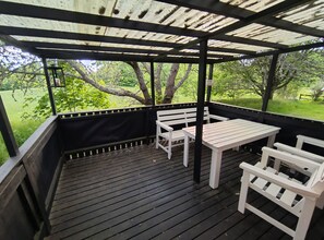 Un'area esterna coperta con un pavimento in legno, panchine bianche e un tavolo.