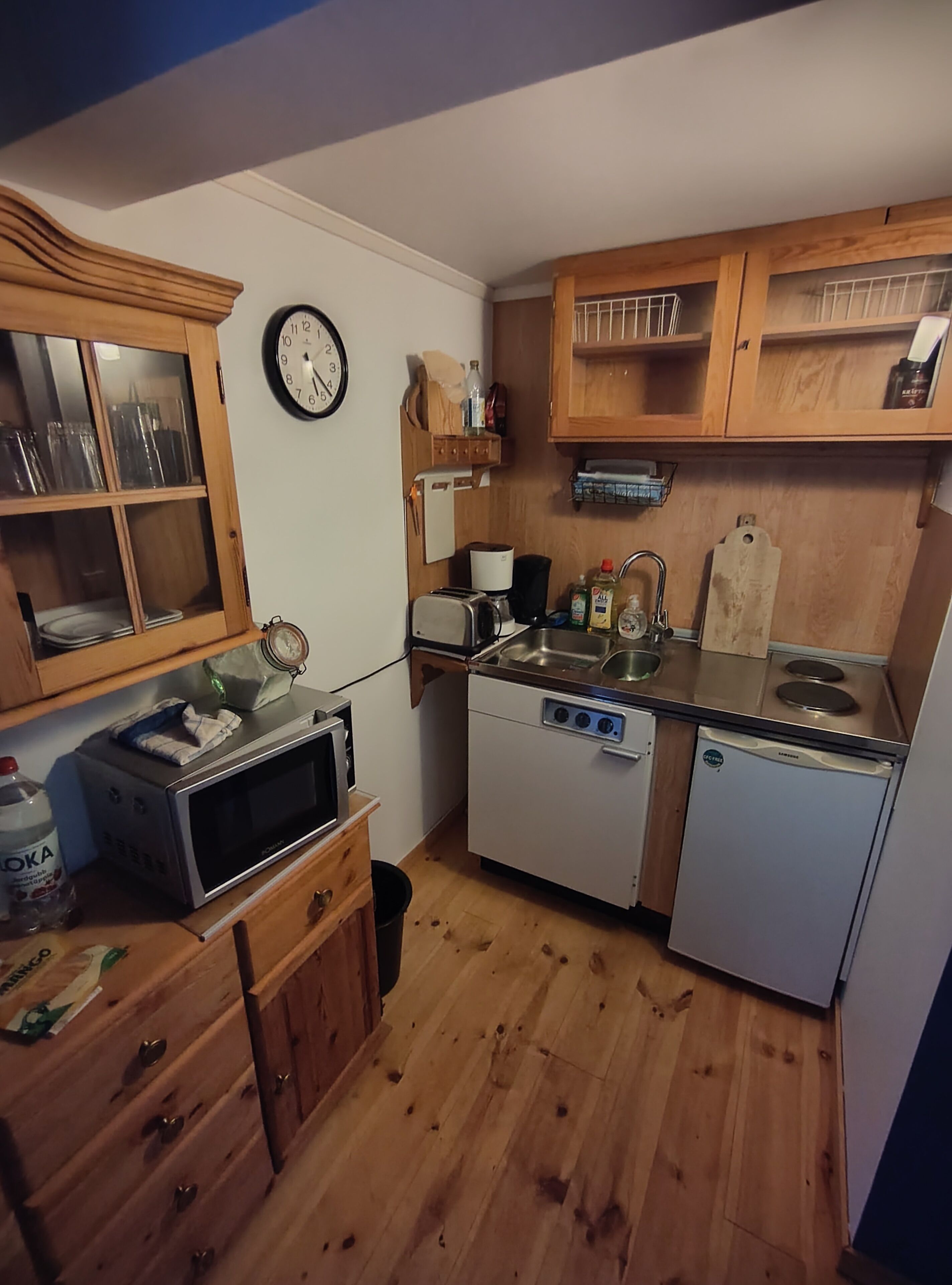 A compact kitchen with wooden cabinets, a microwave, a toaster, a dishwasher, and a sink.