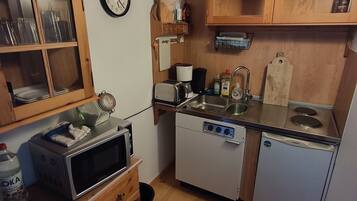 A compact kitchen with wooden cabinets, a microwave, a toaster, a dishwasher, and a sink.