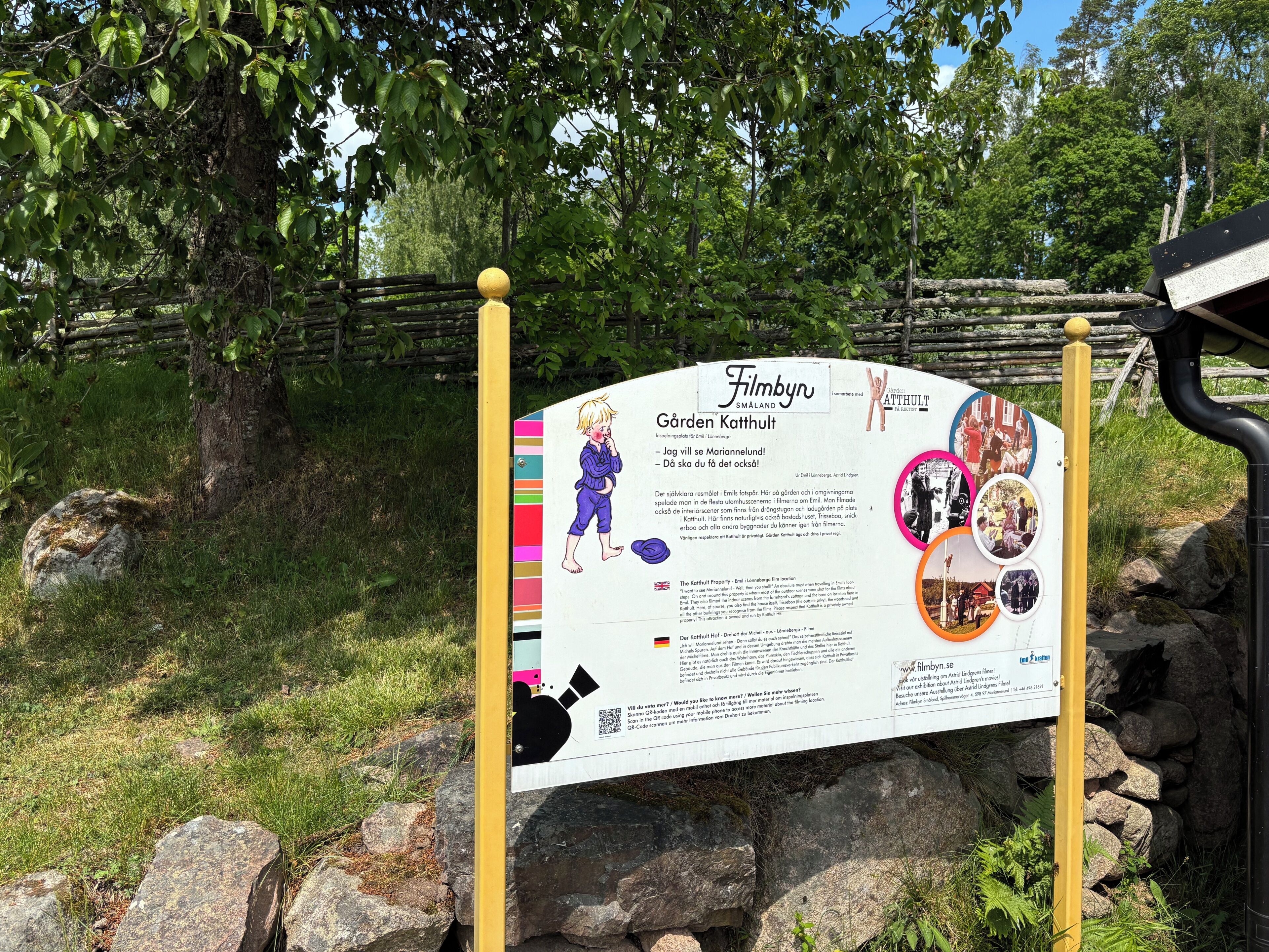 A signboard with text and images, surrounded by trees and rocks.