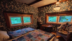 Una habitación con dos camas, una silla, una mesita y una ventana que da a zonas verdes.
