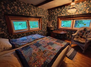 Een kamer met twee bedden, een stoel, een klein tafeltje en een raam met uitzicht op groen.