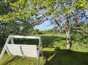 A white swing set in a grassy field with trees in the background.