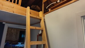 Un dormitorio tipo loft con una escalera de madera, una cama litera y una puerta visible que da a otra habitación.