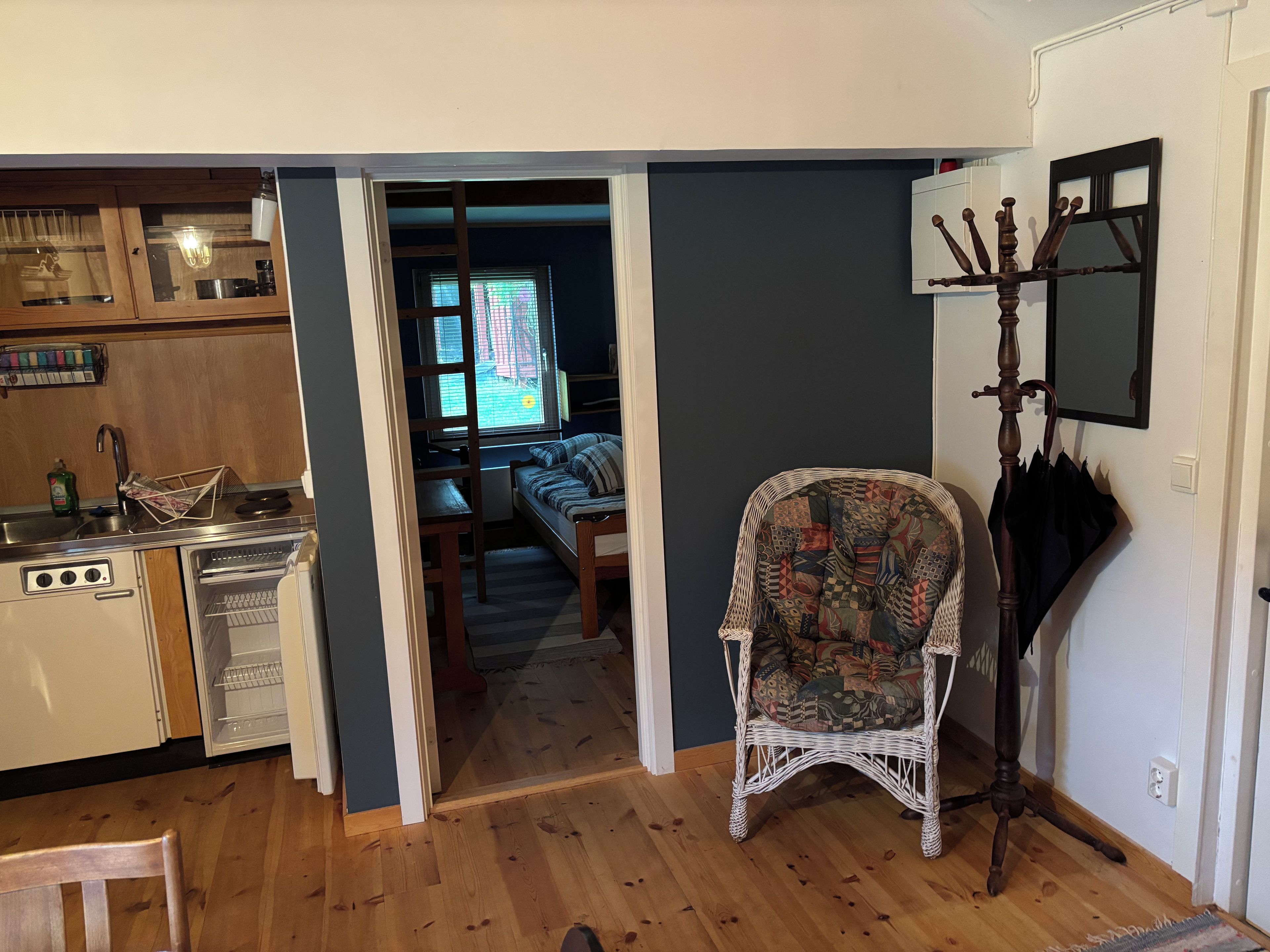 A compact kitchen with a dining area, a wicker chair, and a coat rack.
