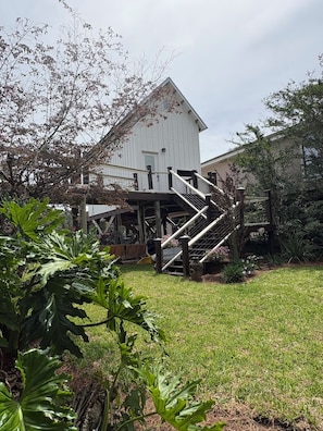 A white building with a staircase leading to a porch, surrounded by greenery and a grassy lawn.