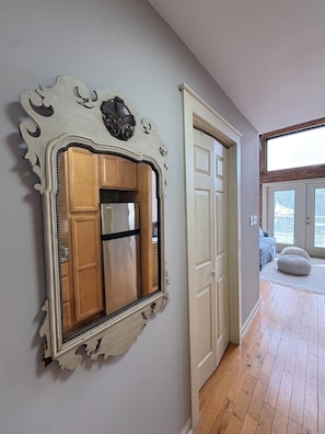 A room with a large mirror, wooden cabinets, a door, and a view through a window.