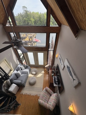 A room with a large window, a ceiling fan, a sofa, a chair, a rug, and wall art.