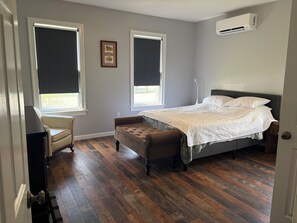 Ein Schlafzimmer mit einem Bett, einer Sitzbank, zwei Fenstern und einer Klimaanlage.