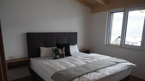 A bedroom with a bed, a headboard, a nightstand, a window, and a view of the outside. - Glungezer vacation apartment (Thaur)