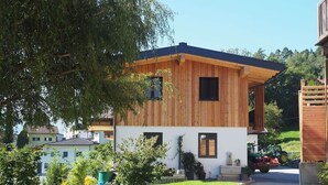 A modern two-story building with a wooden facade, a paved driveway, and a green lawn. - Glungezer vacation apartment (Thaur)