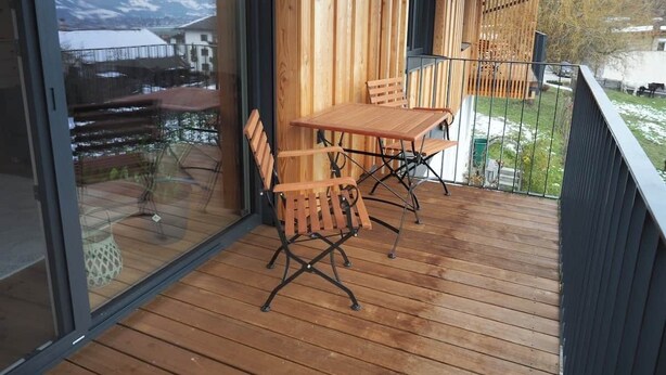 Eine Holzdachterrasse mit Tisch und Stühlen, einer Glastür und Blick auf einen Berg.
