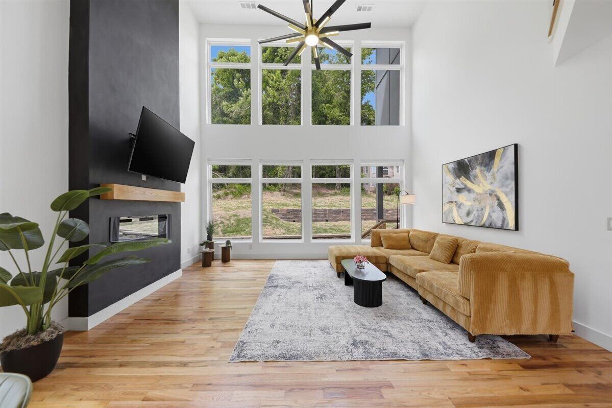 A modern living room with a large window, a flat-screen TV, a sofa, a coffee table, and a ceiling fan.