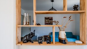 Une étagère en bois ornée d’objets décoratifs, un vase contenant des plantes séchées et, au fond, un canapé bleu.