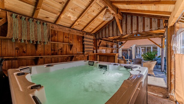 Un espace de détente en bois comprenant un jacuzzi, des poutres en bois et des meubles en osier.