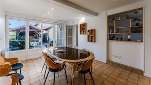 Un espace repas avec une table à plateau de verre, des chaises en bois et une vue sur une terrasse extérieure, accessible par de grandes fenêtres.