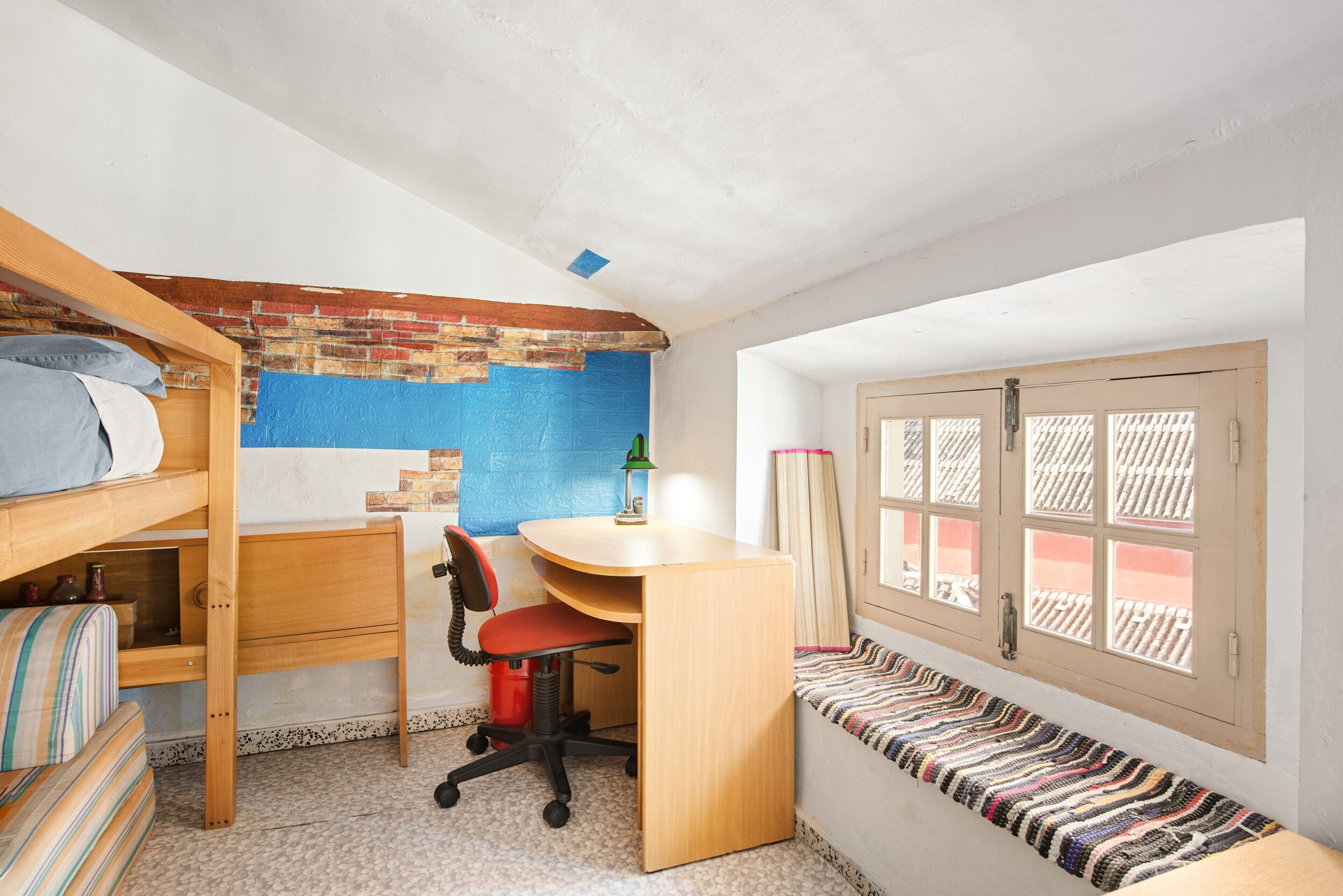 Quarto estilo dormitório com beliche, escrivaninha, cadeira e janela com vista.