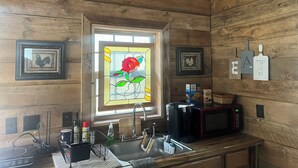 A wooden interior with a kitchen area, including a sink, a microwave, and a window with a stained glass rose.