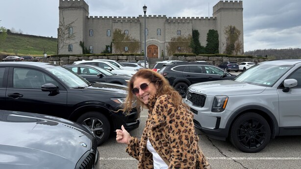 A parking lot with multiple cars, a castle-like building in the background, and a person giving a thumbs-up.