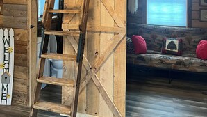 A wooden interior with a ladder leading to a loft area, a welcome sign, and a window with a view.
